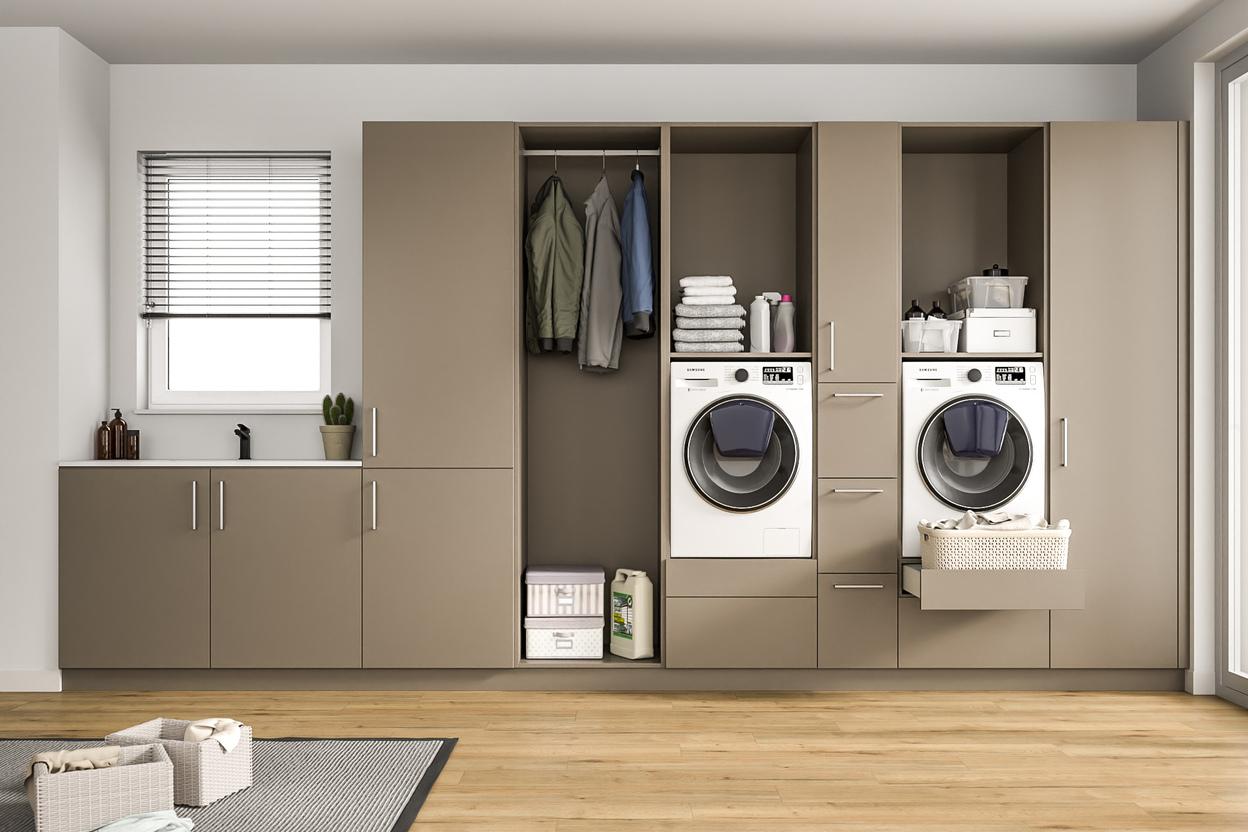 Modern gestalteter Wirtschaftsraum mit massgefertigten Schränken. Ein heller Raum mit einem grossen, massgeschneiderten Schranksystem in Taupe, integrierten Waschmaschinen, Ablageflächen und einem Fenster mit Jalousien.