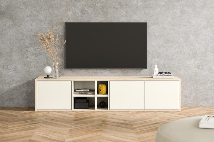 Moderne Kommode nach Mass unter TV im Wohnzimmer Massgefertigte Kommode in Creme mit offenen Fächern und gelben Akzenten, unter einem Wandfernseher, vor einer Betonwand im urbanen Wohnzimmer.