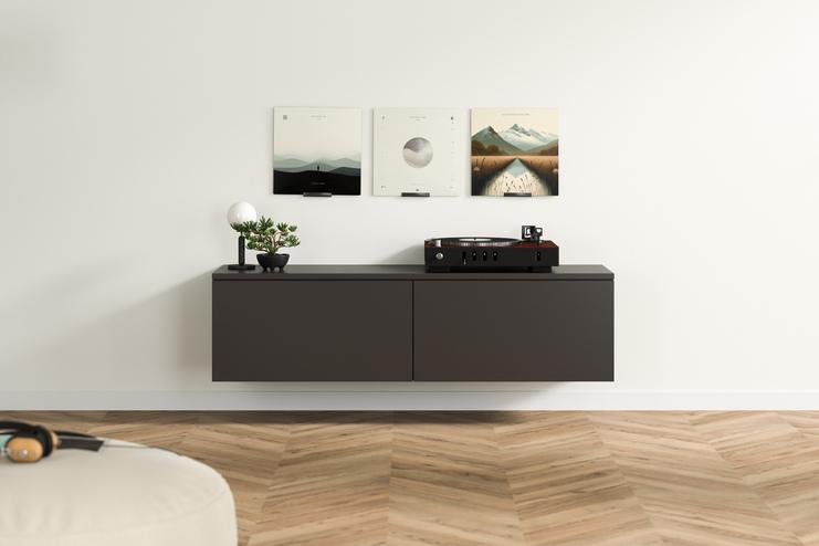Modernes Hängeboard nach Mass mit minimalistischer Ausstrahlung Dunkelgraues, massgefertigtes Hängeboard mit klaren Linien und Plattenspieler, akzentuiert durch eine Pflanze und kunstvolle Bilder an der Wand darüber.